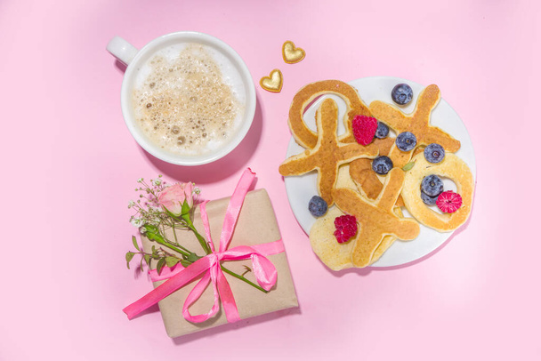 XOXO muotoinen Ystävänpäivä pannukakkuja, marja ja kahvi latte muki vaaleanpunainen tausta kopioi tilaa. Ystävänpäivä makea maukas aamiainen idea - Valokuva, kuva