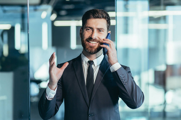 Happy and smiling businessman having fun talking on the phone, man in modern office, close-up portrait photo - Photo, image