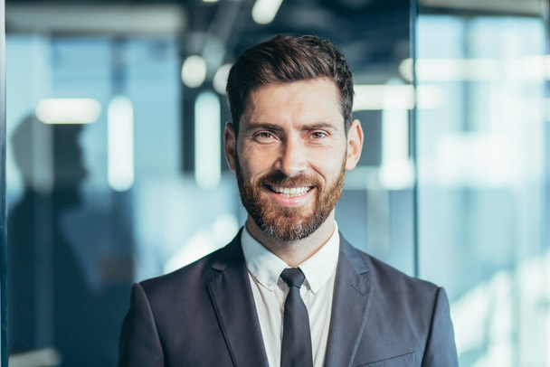 Close-up portrait of businessman with beard looking at camera and smiling, man in modern office - Foto, Imagem