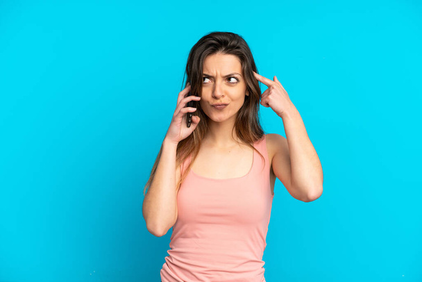 Young caucasian woman using mobile phone isolated on blue background having doubts and thinking - Fotografie, Obrázek