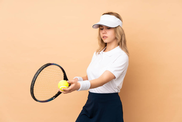 Подростковая русская девушка, изолированная на бежевом фоне, играет в теннис - Фото, изображение