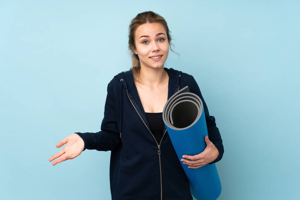Teenager Russian girl holding mat isolated on blue background smiling - Photo, Image