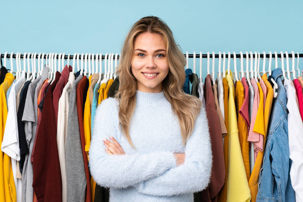 Teenager Russian girl buying some clothes isolated on blue background keeping the arms crossed in frontal position - Foto, Imagem