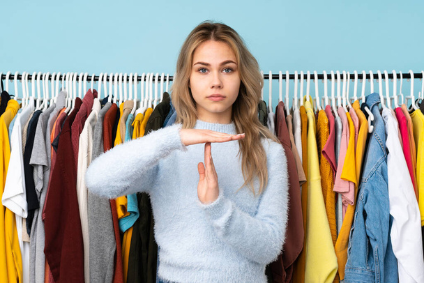 Teenager rusky dívka kupovat nějaké oblečení izolované na modrém pozadí dělat čas ven gesto - Fotografie, Obrázek