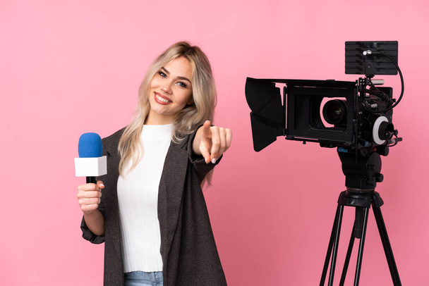 Toimittaja nainen jolla on mikrofoni ja raportointi uutisia yli eristetty vaaleanpunainen tausta osoittaa sormella sinua luottavainen ilme - Valokuva, kuva