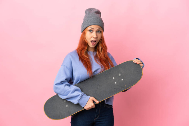 Teenager russische Mädchen isoliert auf rosa Hintergrund mit einem Skate und dabei überraschende Geste - Foto, Bild