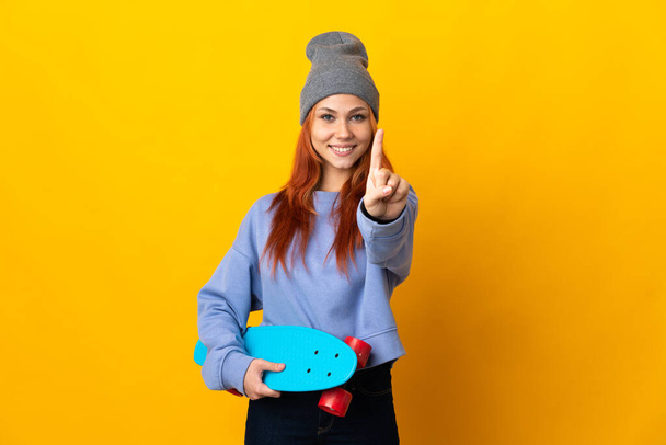 tiener russisch skater meisje geïsoleerd op gele achtergrond tonen en tillen een vinger - Foto, afbeelding