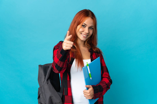 Teenager student Russian girl isolated on blue background pointing to the front and smiling - Фото, изображение