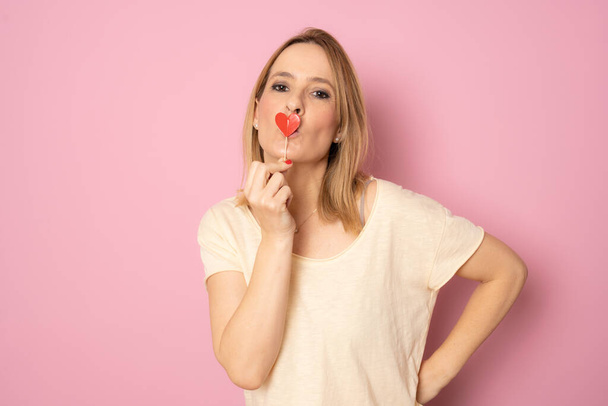 Nemluvná dáma v lásce držet malé srdce karta kryt ústa izolované přes růžové pozadí - Fotografie, Obrázek