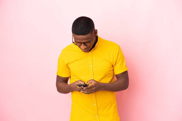 Junger lateinischer Mann isoliert auf rosa Hintergrund sendet eine Nachricht mit dem Handy - Foto, Bild
