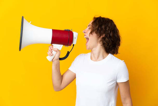 Young English woman isolated on yellow background shouting through a megaphone to announce something in lateral position - Foto, imagen
