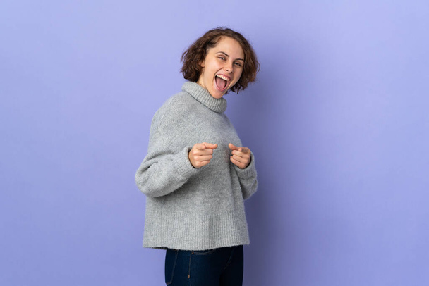 Junge Engländerin auf violettem Hintergrund, die nach vorne zeigt und lächelt - Foto, Bild