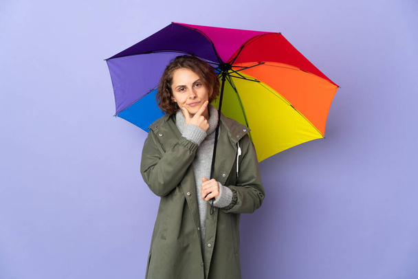 English woman holding an umbrella isolated on purple background thinking - Foto, Imagem