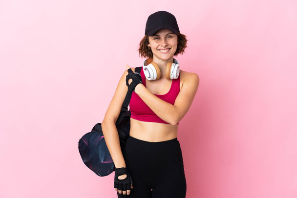 Mujer deportiva joven con bolsa de deporte sobre fondo aislado apuntando a un lado para presentar un producto - Foto, Imagen