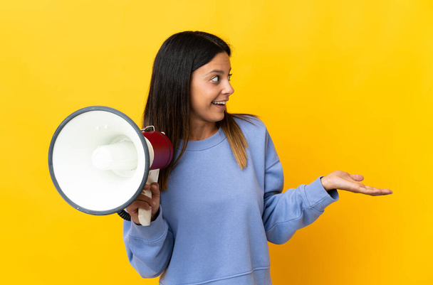 Caucasian girl isolated on yellow background holding a megaphone and with surprise facial expression - Foto, imagen