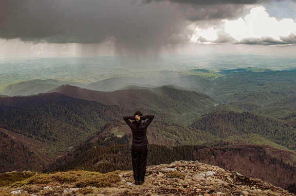 Rear view of a woman standing against the storm in the mountains - Фото, изображение