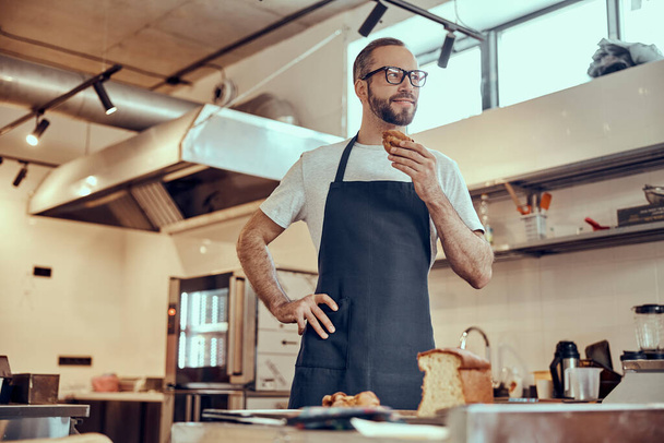 Bearded male baker in apron holding pastry - Zdjęcie, obraz