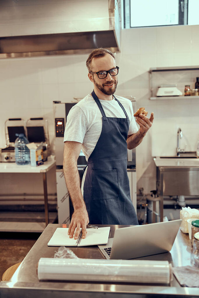 Cheerful male worker standing by the table with laptop in cafe - Foto, Bild