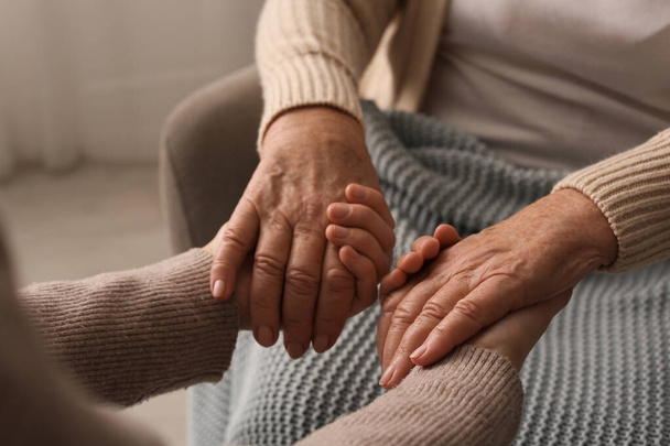 Young and elderly women holding hands together indoors, closeup - Fotografie, Obrázek