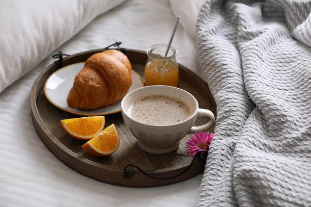 Wooden tray with delicious breakfast and beautiful flower on bed indoors - Фото, зображення