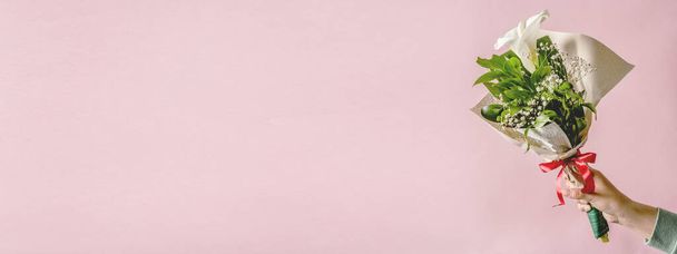 Mãos de mulher caucasiana desconhecida segurando buquê de flor Calla Zantedeschia decorada na frente de fundo rosa ou parede - celebração de congratulações e conceito de ocasião especial com espaço de cópia - Foto, Imagem