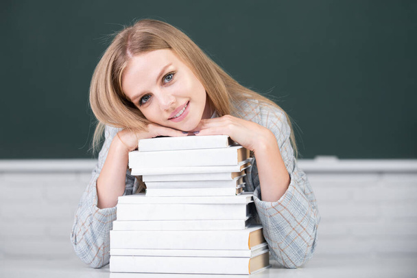 Primer plano retrato de la joven estudiante atractiva feliz con libros en el fondo de pizarra con espacio de copia. - Foto, imagen