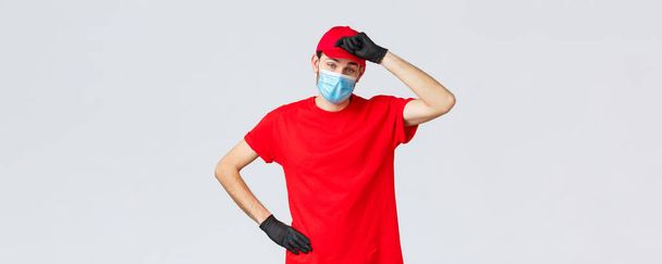 Covid-19, самокарантин, онлайн концепція шопінгу. Доставити хлопця, що витирає піт з чола, як втомився нести важкі пакети для клієнтів, працюючи в спалаху коронавірусу, носити маску для обличчя і рукавички
 - Фото, зображення