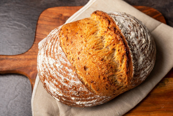 Wholemeal sourdough bread on linen napkin on brown wooden chopping board. - Foto, Bild