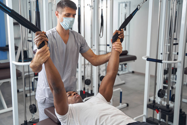 Male patient working out on gym equipment supervised by physiotherapist - Фото, зображення