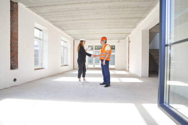 Woman construction engineer shaking hands with worker in room - Φωτογραφία, εικόνα