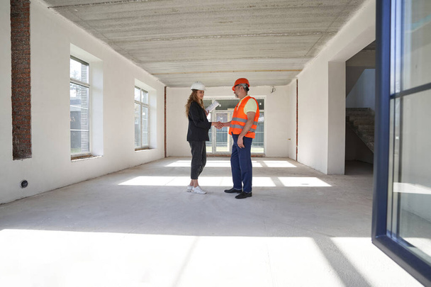 Pleased woman designer giving handshake to construction worker indoors - Photo, image