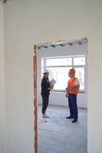 Builder and woman designer with coffee talking in room - Фото, зображення