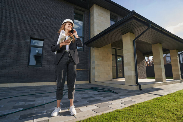 Happy woman engineer having a call in front of house - Photo, Image
