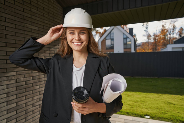 Female engineer adjusting her helmet near house entrance - Foto, Imagen