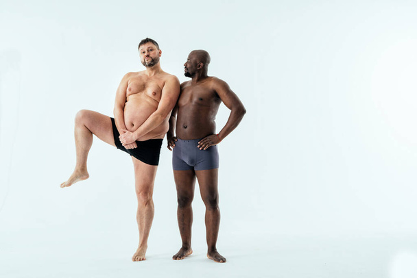 two multiethnic men posing for a male edition body positive beauty set. Shirtless guys with different age, and body wearing boxers underwear - Foto, Imagem