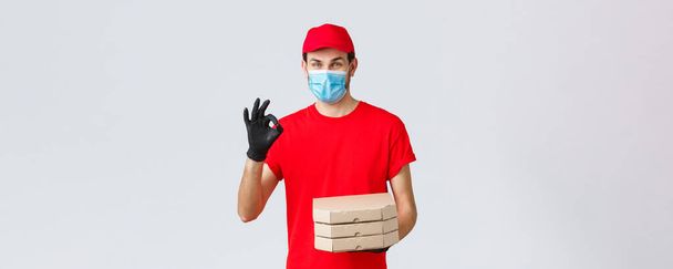 Food delivery, application, online grocery, contactless shopping and covid-19 concept. Courier guarantee quality of pizza, holding boxes, showing okay sign in recommendation or approval, wear mask - Photo, Image