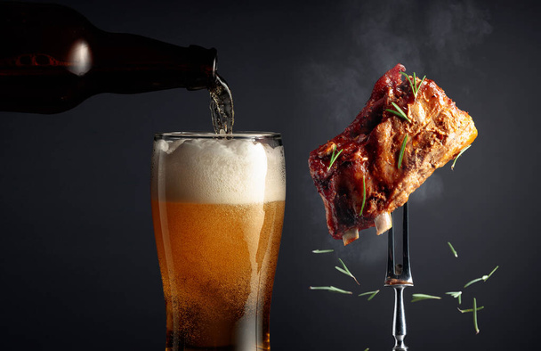 Μπύρα και παϊδάκια στη σχάρα. Ψητό κρέας πασπαλισμένο με δενδρολίβανο σε μαύρο φόντο. - Φωτογραφία, εικόνα