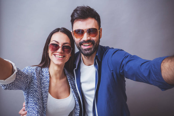 Young beautiful couple making self in glasses on a gray background - Foto, immagini
