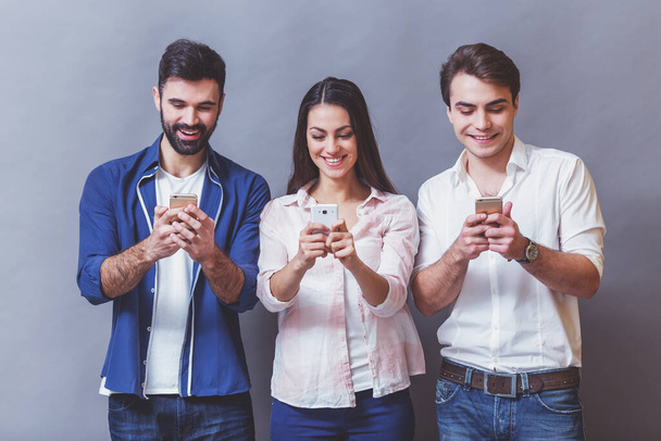 Koncepce technologií a Internetu: skupina mladých lidí, kteří se dívají na své telefony, na šedém pozadí - Fotografie, Obrázek
