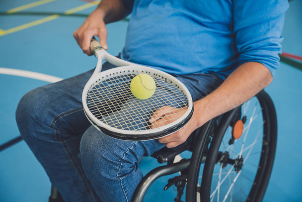 Adult man with a physical disability who uses wheelchair playing tennis on indoor tennis court - 写真・画像