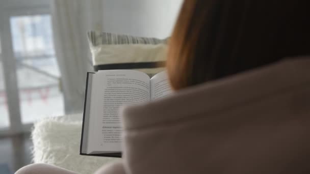 valkoinen sisustus, tyttö lukee kirjaa ja kääntää sivut takaisin näkymä - Materiaali, video