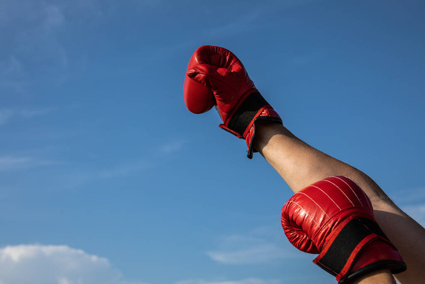 Фотографія високої роздільної здатності чоловічої руки, що тримає червоні боксерські рукавички на хмарному блакитному небі
. - Фото, зображення