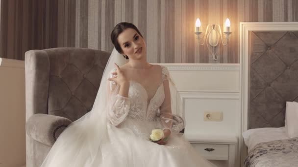 Mariée fille en robe blanche assis sur la chaise dans la chambre à coucher avec des fleurs bouquet de mariage pour marié - Séquence, vidéo