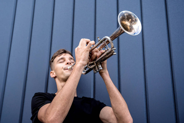 Young street musician playing the trumpet near the big blue wall - Fotoğraf, Görsel