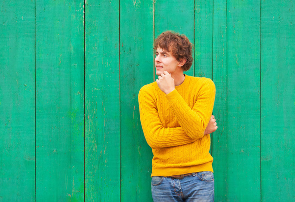 thinking curly man in yellow sweater and scarf on green wooden b - Fotografie, Obrázek