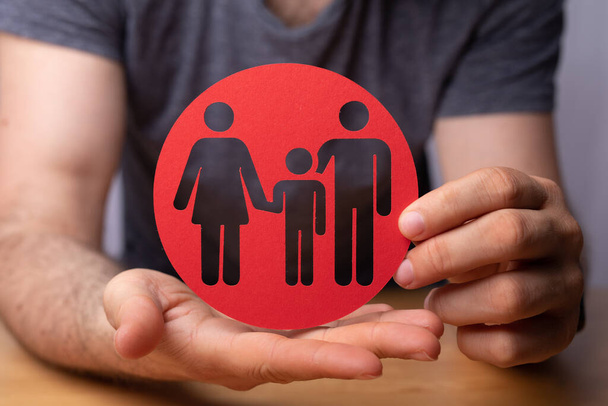 A closeup of a person holding a round red sign with family figures - family insurance concept - Фото, зображення
