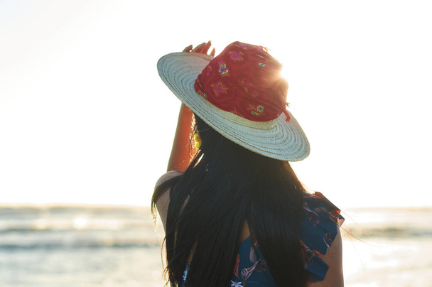 Una vista trasera de una mujer hispana usando un sombrero de verano bajo el sol en la playa - Foto, imagen