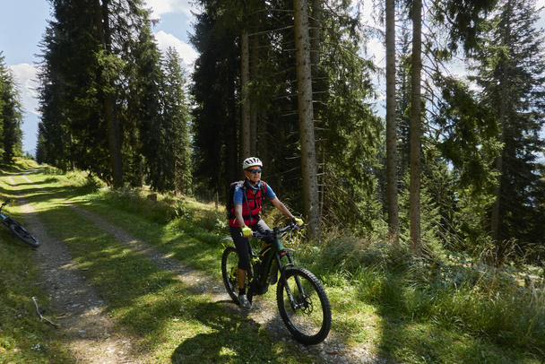 An elderly lady riding her bike through the woods on a beautiful sunny day in Switzerland - Fotografie, Obrázek