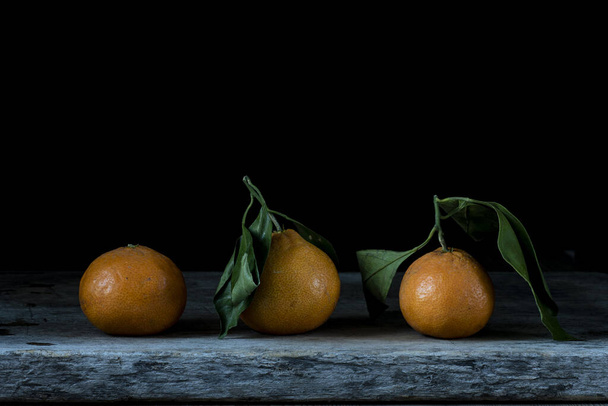 A closeup shot of fresh mandarins with green leaves on a wooden table - Foto, afbeelding