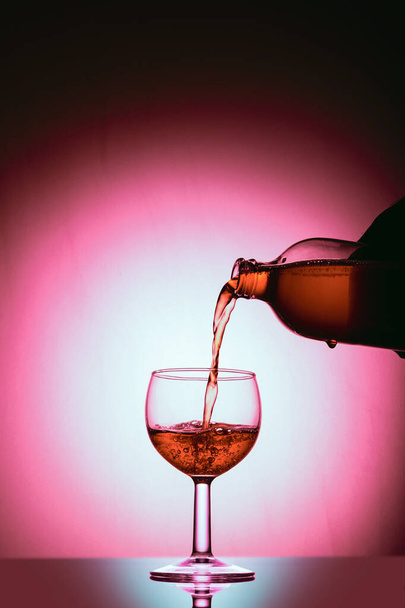 Pouring wine into a glass; an object in the red spotlight - Foto, afbeelding